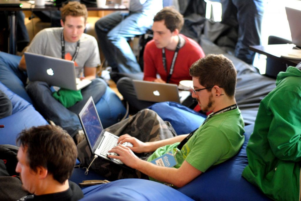 A group of men sit on beanbags working on their laptops